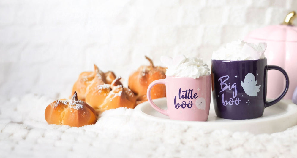 Two Halloween-themed mugs with pumpkins and whipped cream on a white background
